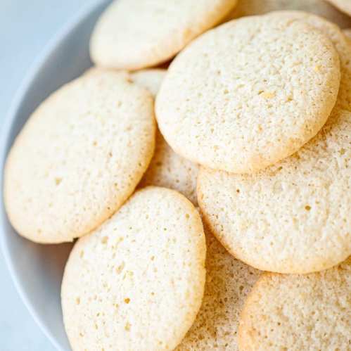 A close-up of a bowl filled with golden, round cookies stacked together.