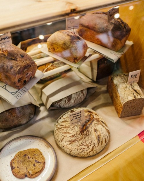 A display case filled with various types of bread, including loaves and cookies, labeled with tags.