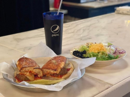 A plate with two stuffed sandwiches, a side salad, and a Pepsi drink on a marble countertop.