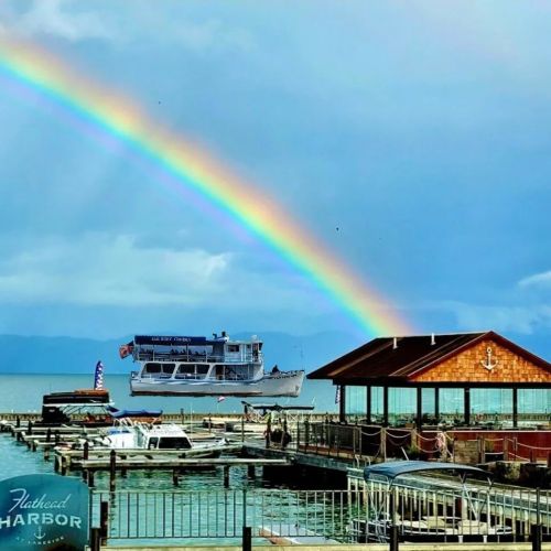 A boat near a dock under a vibrant rainbow, with calm waters and a cloudy sky in the background.