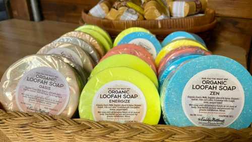 A basket filled with colorful organic loofah soaps labeled "Oasis," "Energize," and "Zen."