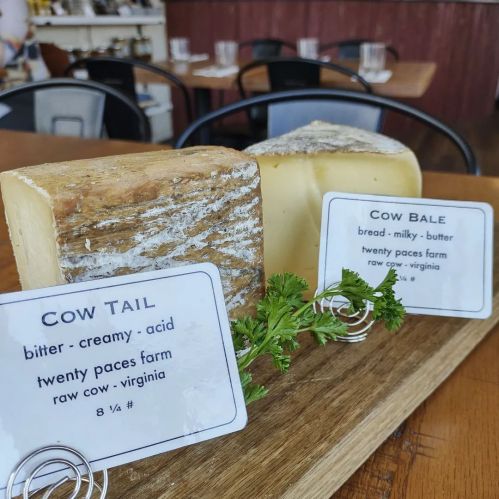 Two cheese blocks on a wooden board with labels: "Cow Tail" and "Cow Bale," garnished with parsley.