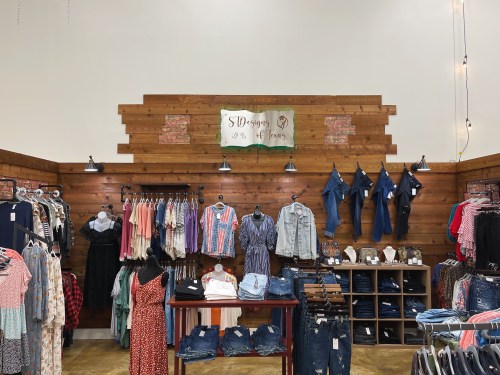 A clothing store display featuring racks of apparel, denim, and accessories against a wooden wall backdrop.