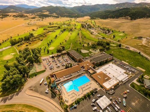 Aerial view of a hotel with a large pool, surrounded by green golf courses and rolling hills under a cloudy sky.