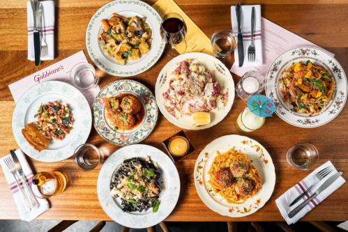 A variety of colorful pasta dishes arranged on a wooden table, with drinks and utensils nearby.