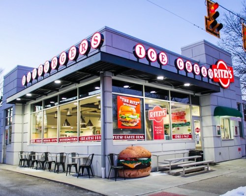 A modern restaurant exterior featuring a sign for "Ritz's Burgers & Ice Cream," with outdoor seating and a large burger sculpture.