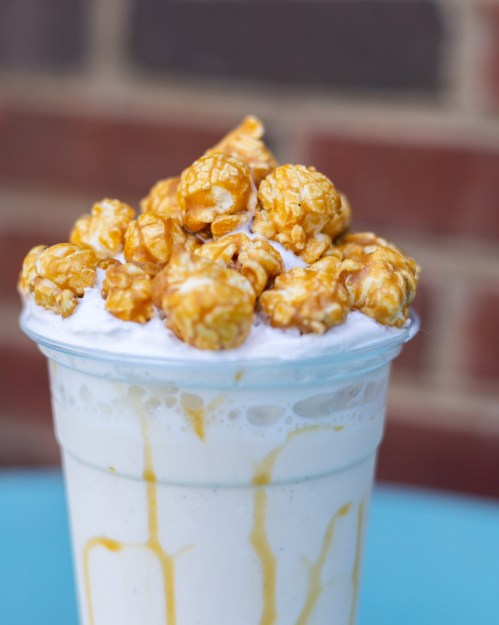 A creamy milkshake topped with caramel popcorn and drizzled with caramel sauce, served in a clear cup.