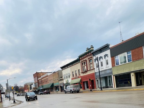 A quiet street scene featuring historic buildings, shops, and a cloudy sky in a small town.