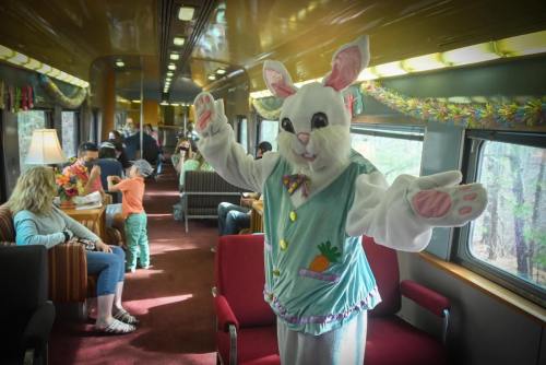 A person in a bunny costume waves inside a vintage train car filled with families and children.