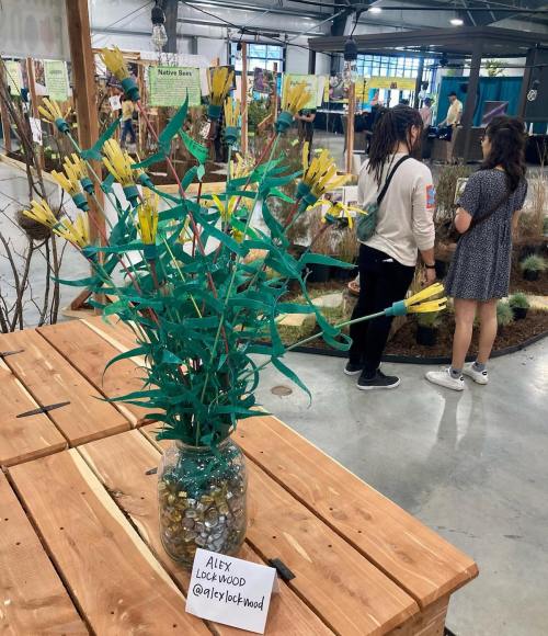 A vibrant flower arrangement made of yellow and green materials in a glass vase, displayed on a wooden table.