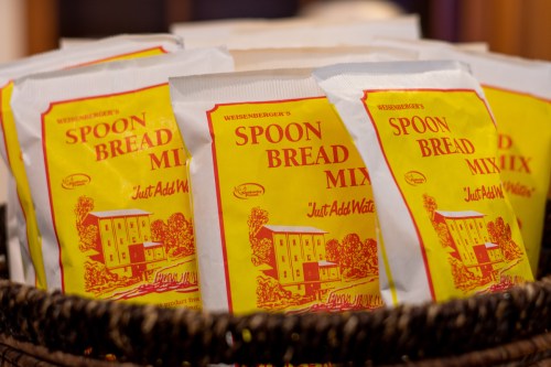 A basket filled with packets of Weisenberger's Spoon Bread Mix, featuring a yellow design and the text "Just Add Water."