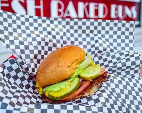 A delicious sandwich with lettuce, pickles, and ham, served in a checkered paper basket.