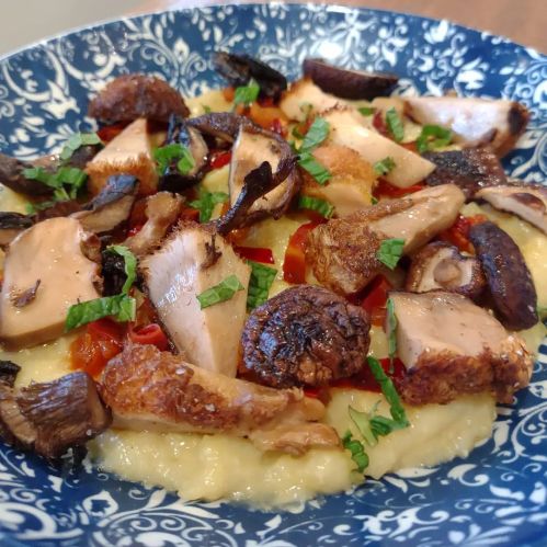 A blue patterned bowl filled with creamy polenta topped with sautéed mushrooms, chicken, and fresh herbs.