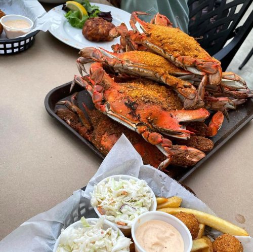 A platter of seasoned crabs with sides of coleslaw, fries, and a seafood ball on a table.