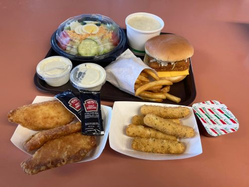 A tray with a salad, chicken sandwich, fries, fish fillets, and mozzarella sticks, accompanied by dipping sauces.