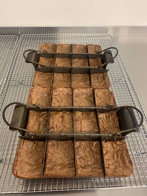 A metal brownie pan with dividers, holding freshly baked brownies on a cooling rack.