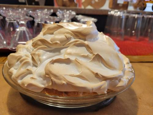 A close-up of a meringue-topped pie in a glass dish, with a smooth, fluffy texture and golden-brown peaks.