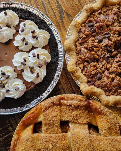 Three delicious desserts: a chocolate cream pie, a pecan pie, and an apple pie with a lattice crust, all on wooden table.