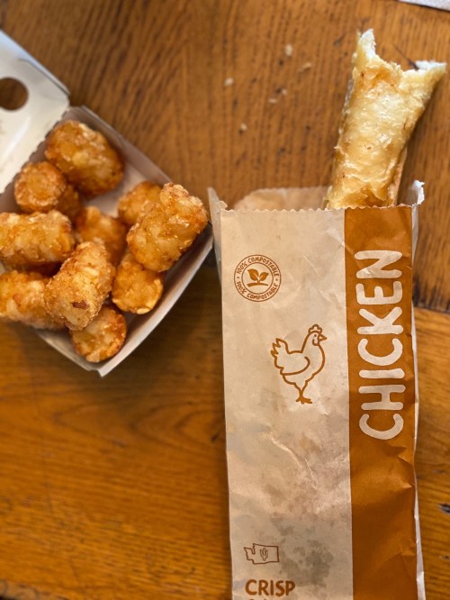 A box of crispy tater tots next to an open container labeled "CHICKEN" with a piece of chicken inside.
