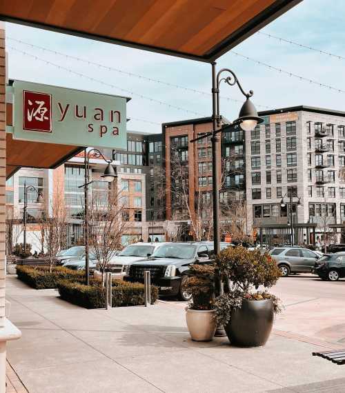 Exterior view of Yuan Spa with modern buildings and parked cars in the background, under a clear sky.