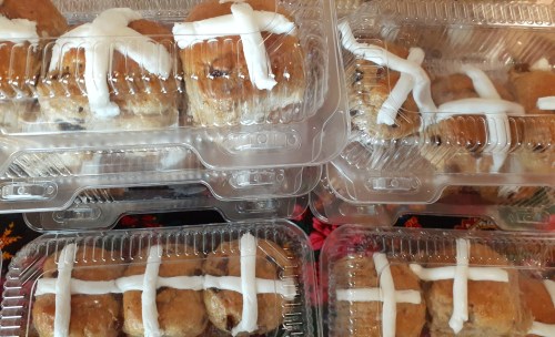A close-up of packaged hot cross buns with white icing crosses on top, arranged in clear plastic containers.