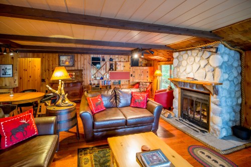 Cozy cabin living room with wooden walls, stone fireplace, leather sofas, and rustic decor. Warm and inviting atmosphere.