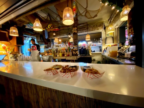A bar counter with three food baskets in front, colorful decor, and a bartender in the background.