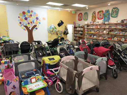 A colorful store filled with various strollers, toys, and baby gear, with a tree mural on the wall.