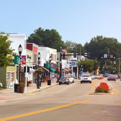 A charming small town street with shops, flowers, and traffic lights on a sunny day.