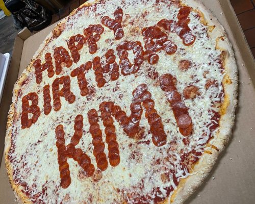 A large pizza topped with cheese and pepperoni, decorated with "Happy Birthday Kim!" written in pepperoni.