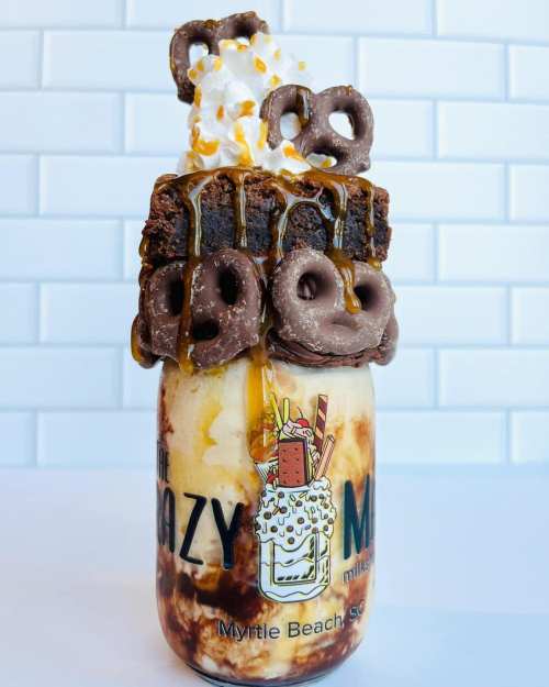 A decadent milkshake topped with brownies, pretzels, whipped cream, and caramel, served in a mason jar.