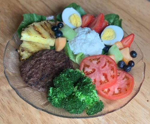 A colorful plate featuring a burger patty, grilled pineapple, boiled eggs, mixed fruits, lettuce, and broccoli.