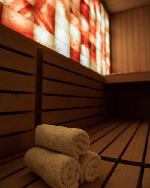 A cozy sauna interior with wooden benches and neatly rolled white towels stacked on the floor.