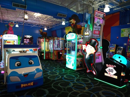 Colorful arcade with various games, including a police car ride and a Monopoly game, in a vibrant indoor space.