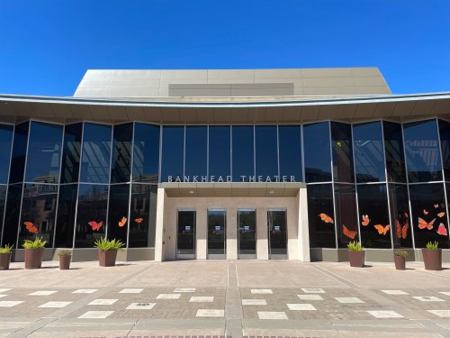 Front view of Bankhead Theater with large glass windows and butterfly decorations on the entrance. Clear blue sky above.