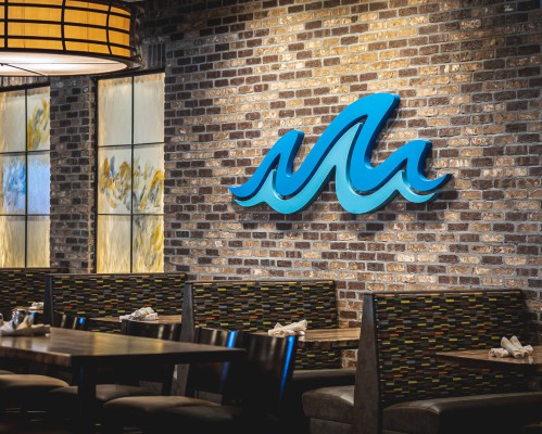 A restaurant interior featuring a brick wall with a blue wave sign and cozy seating arrangements.