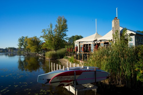 A serene lakeside scene featuring a paddleboard, restaurant, and lush greenery under a clear blue sky.