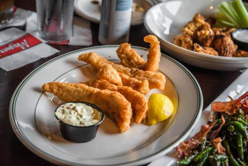 A plate of golden fried fish fillets with a lemon wedge and a small cup of tartar sauce.