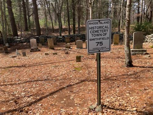 Sign marking a historical cemetery in Smithfield, Rhode Island, surrounded by gravestones and wooded area.