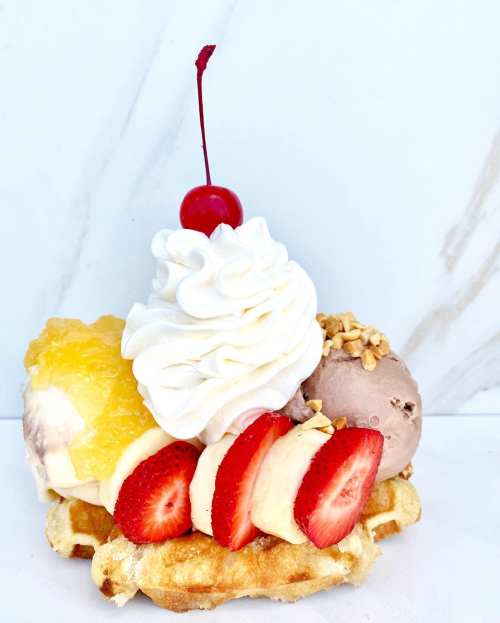 A delicious dessert featuring a waffle topped with ice cream, strawberries, banana slices, whipped cream, and a cherry.