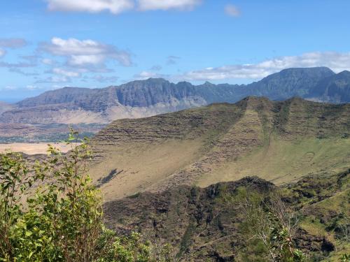A panoramic view of lush green mountains under a blue sky with scattered clouds.