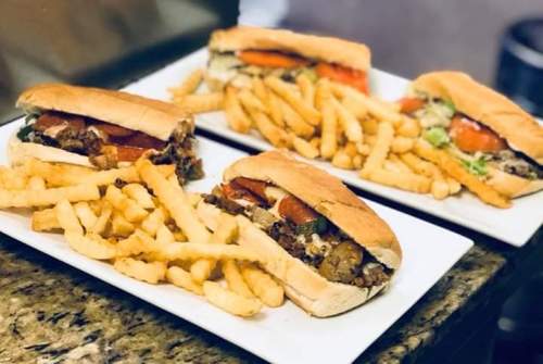 Three sandwiches filled with meat, tomatoes, and lettuce, served with a side of golden French fries on white plates.