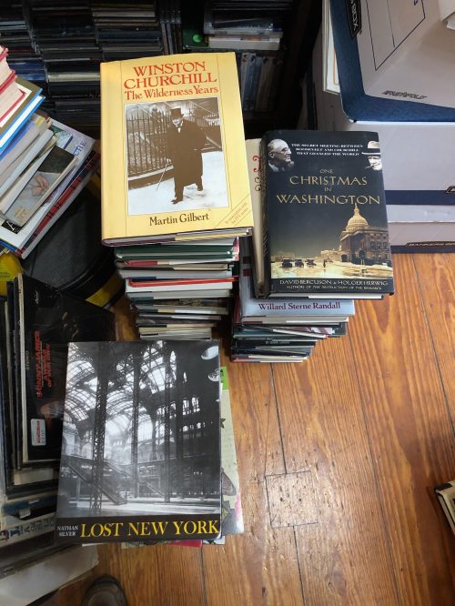 A stack of books, including titles about Winston Churchill and Christmas in Washington, on a cluttered surface.