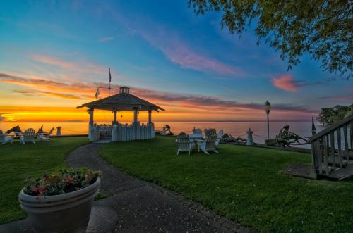 A serene lakeside scene at sunset, featuring a gazebo, chairs, and vibrant sky colors reflecting on the water.