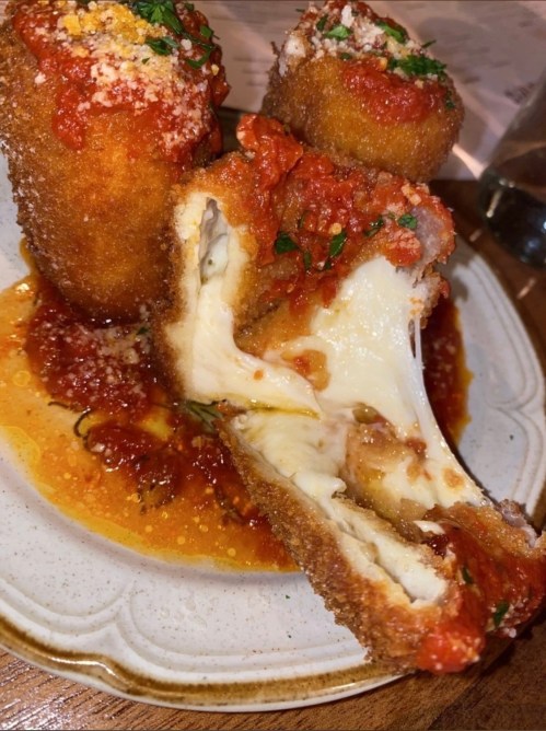 Crispy fried cheese balls drizzled with marinara sauce, showcasing gooey melted cheese inside.