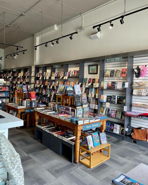 A cozy bookstore interior with shelves of books, tables displaying new titles, and soft lighting.