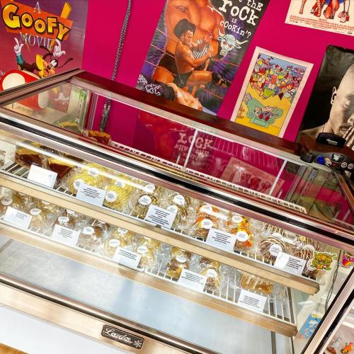 A display case filled with various desserts, set against a vibrant pink wall adorned with colorful posters.