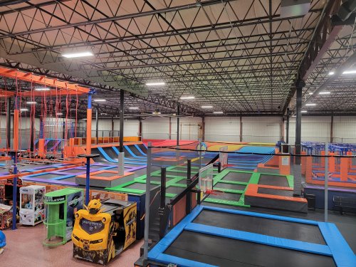 A spacious indoor trampoline park featuring colorful trampolines, climbing walls, and arcade games.