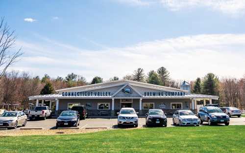 Connecticut Valley Brewing Company building with cars parked outside, set against a clear blue sky and green grass.