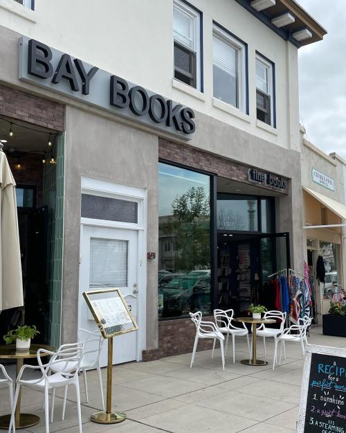 Exterior of Bay Books, featuring a modern storefront with seating outside and a menu board on the sidewalk.